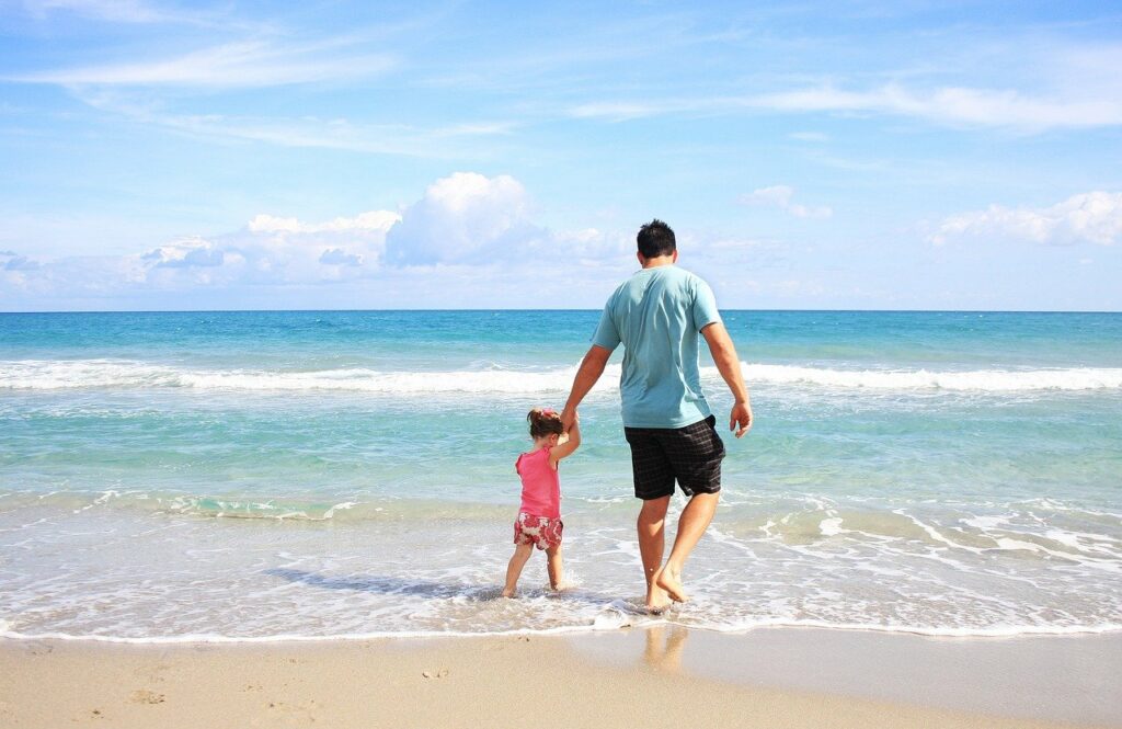 A father walking with his daughter on the beach.